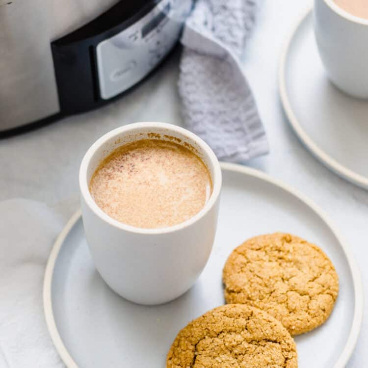 Crock pot filled with pumpkin spice latte recipe and two mugs and cookies too