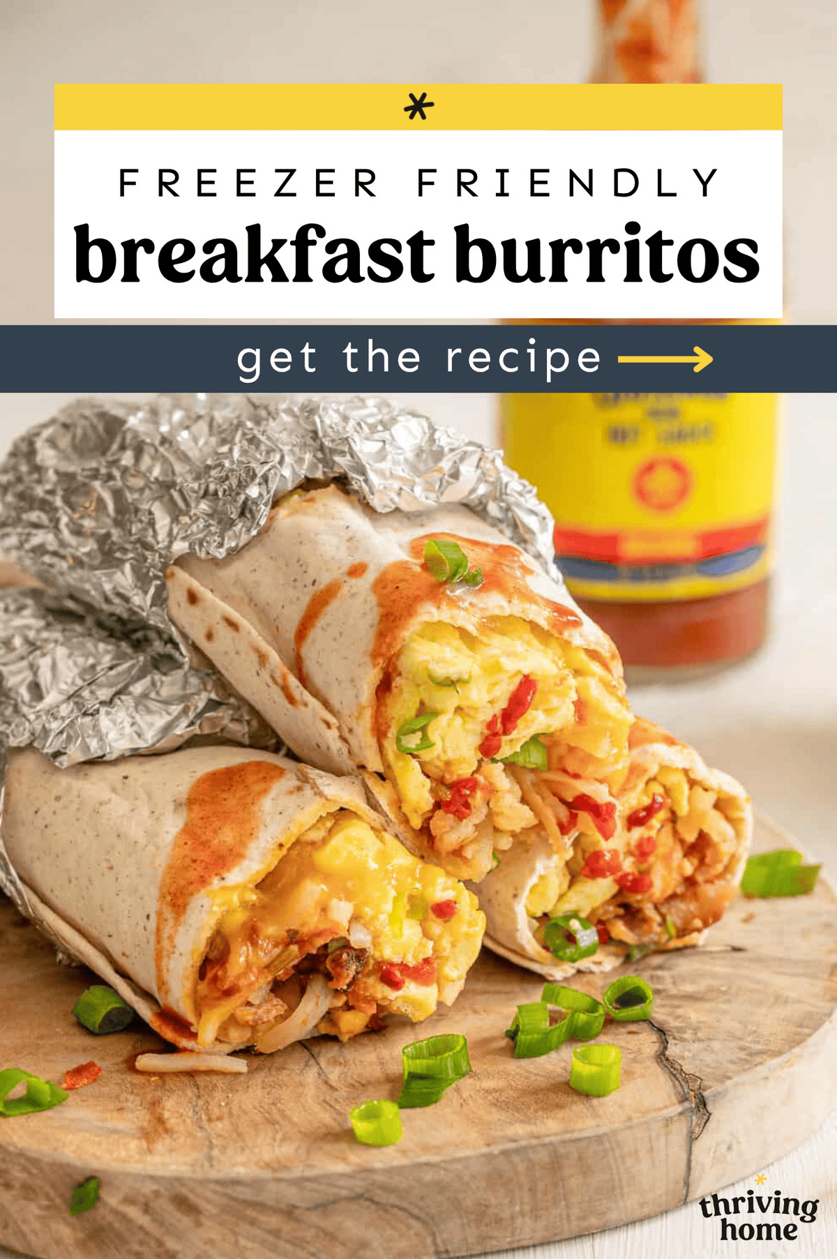 Breakfast burritos wrapped halfway with foil stacked on a cutting board.