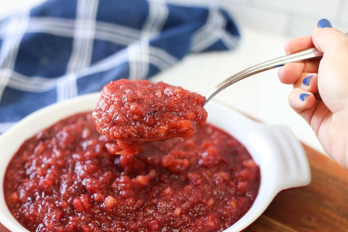 A spoon scooping a serving of apple cranberry sauce. 