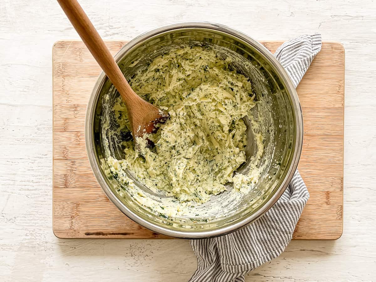 Eggs, shredded mozzarella, grated Parmesan, ricotta cheese, Italian seasoning, salt, pepper, and fresh parsley and basil all mixed together in a mixing bowl.