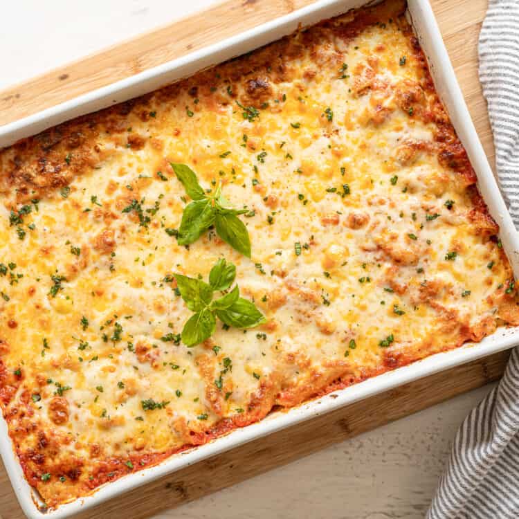 A 9x12 baking dish of cheesy baked pasta with fresh basil on top ready to serve.