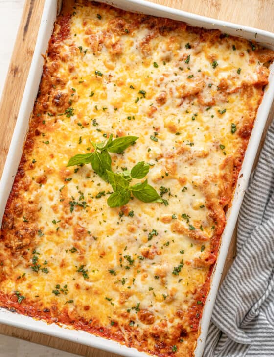 Cheesy baked pasta in a white casserole dish with fresh basil on top.