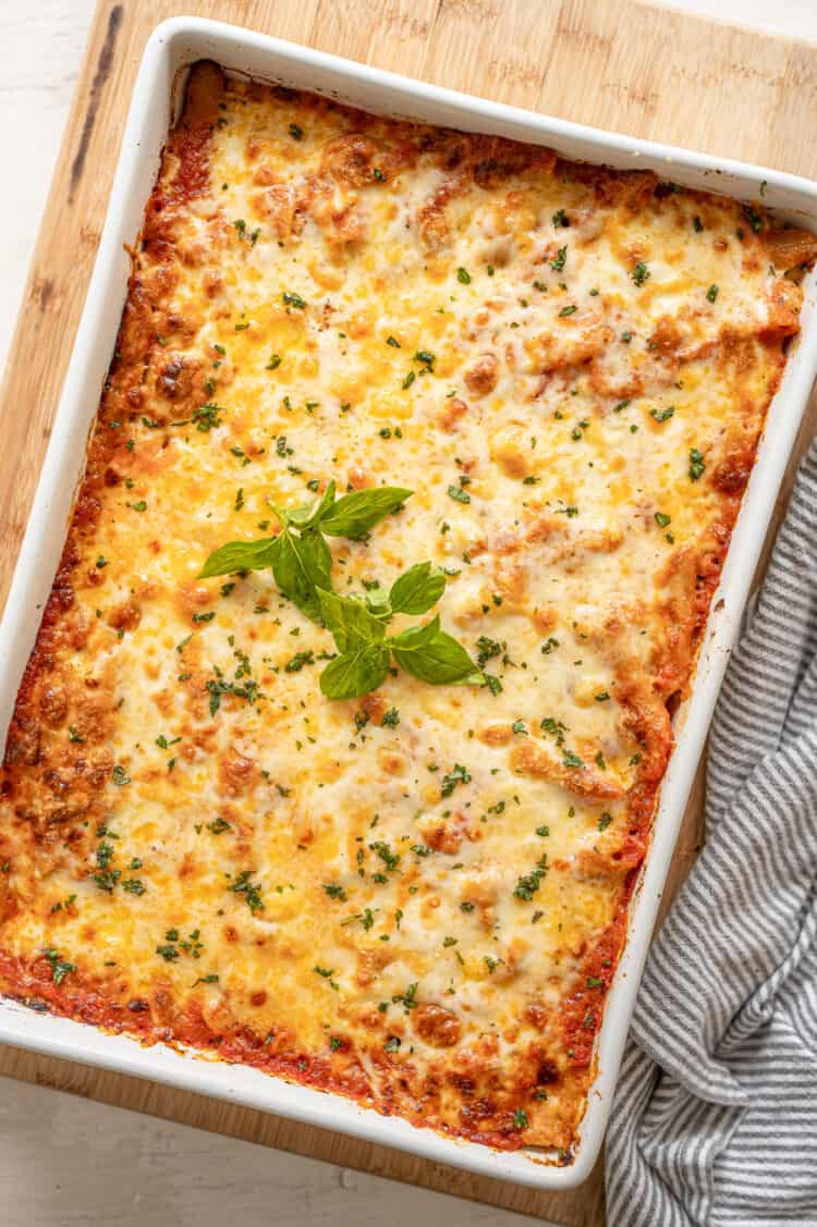 Cheesy baked pasta in a white casserole dish with fresh basil on top.