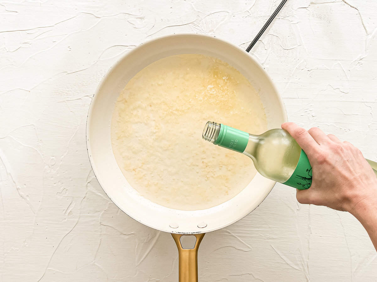 White wine being poured into a frying pan with butter and garlic.
