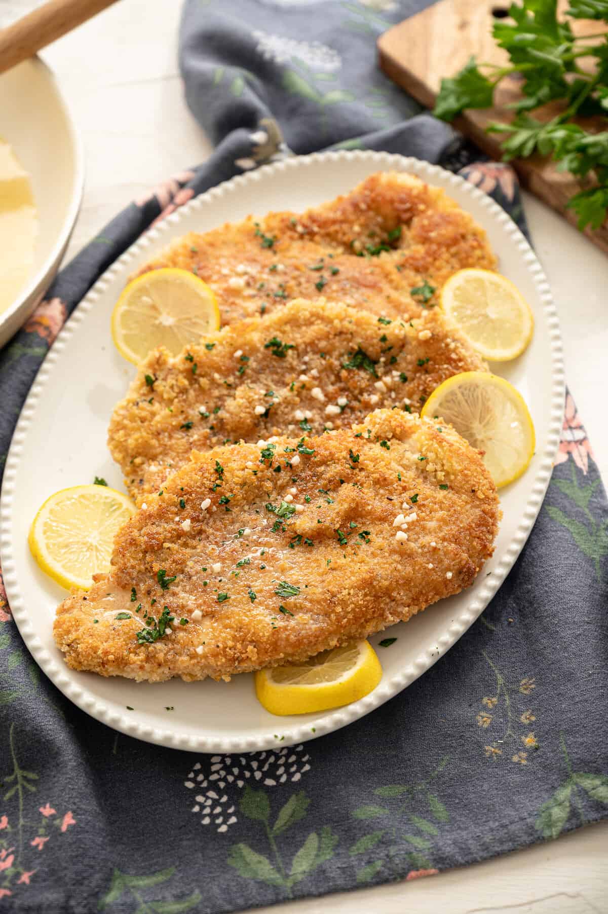 Crispy chicken cutlets on a white serving platter with lemon slices around.