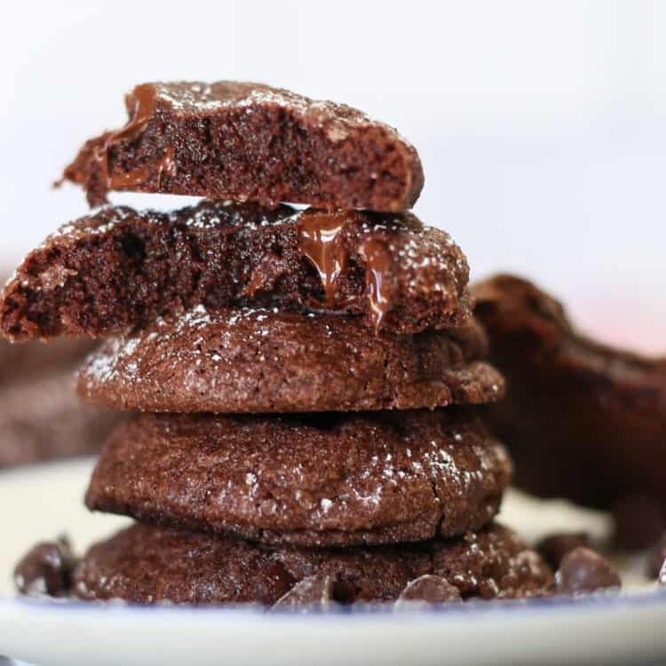 A stack of brownie mix cookies on a plate with one broke in half and melted chocolate dripping down.