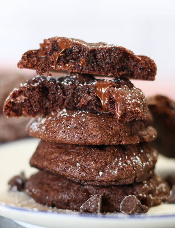 Brownie mix cookies stacked on a plate with melted chocolate dripping off one that has been broken in half.