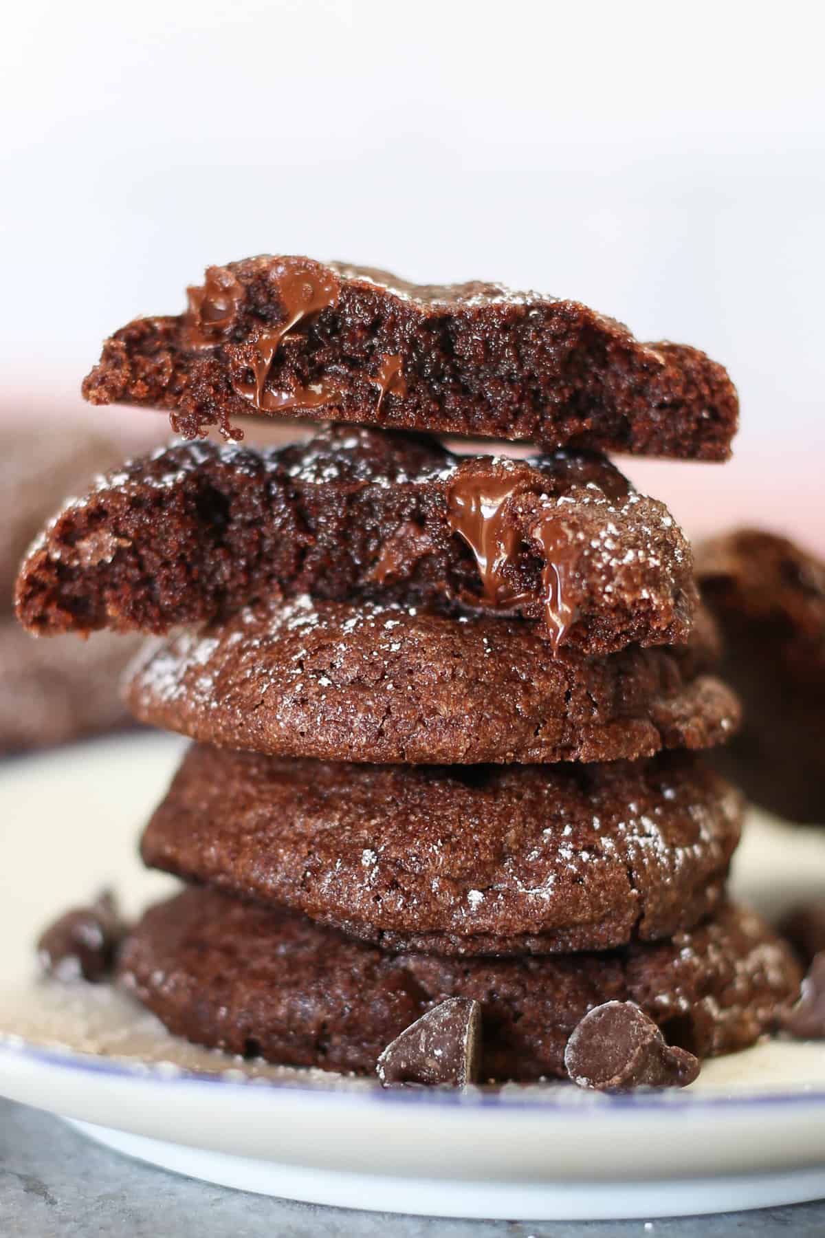 Brownie mix cookies stacked on a plate with melted chocolate dripping off one that has been broken in half.