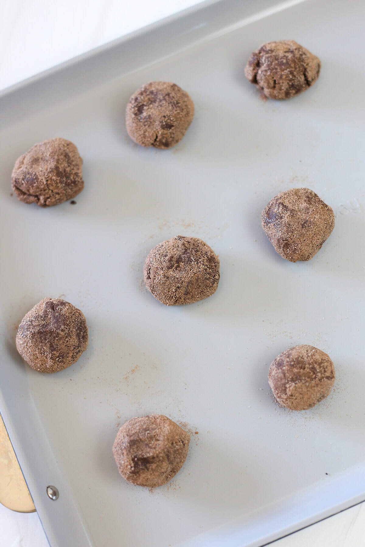 Brownie mix cookie dough balls rolled in cocoa and sugar lined up on a baking sheet.