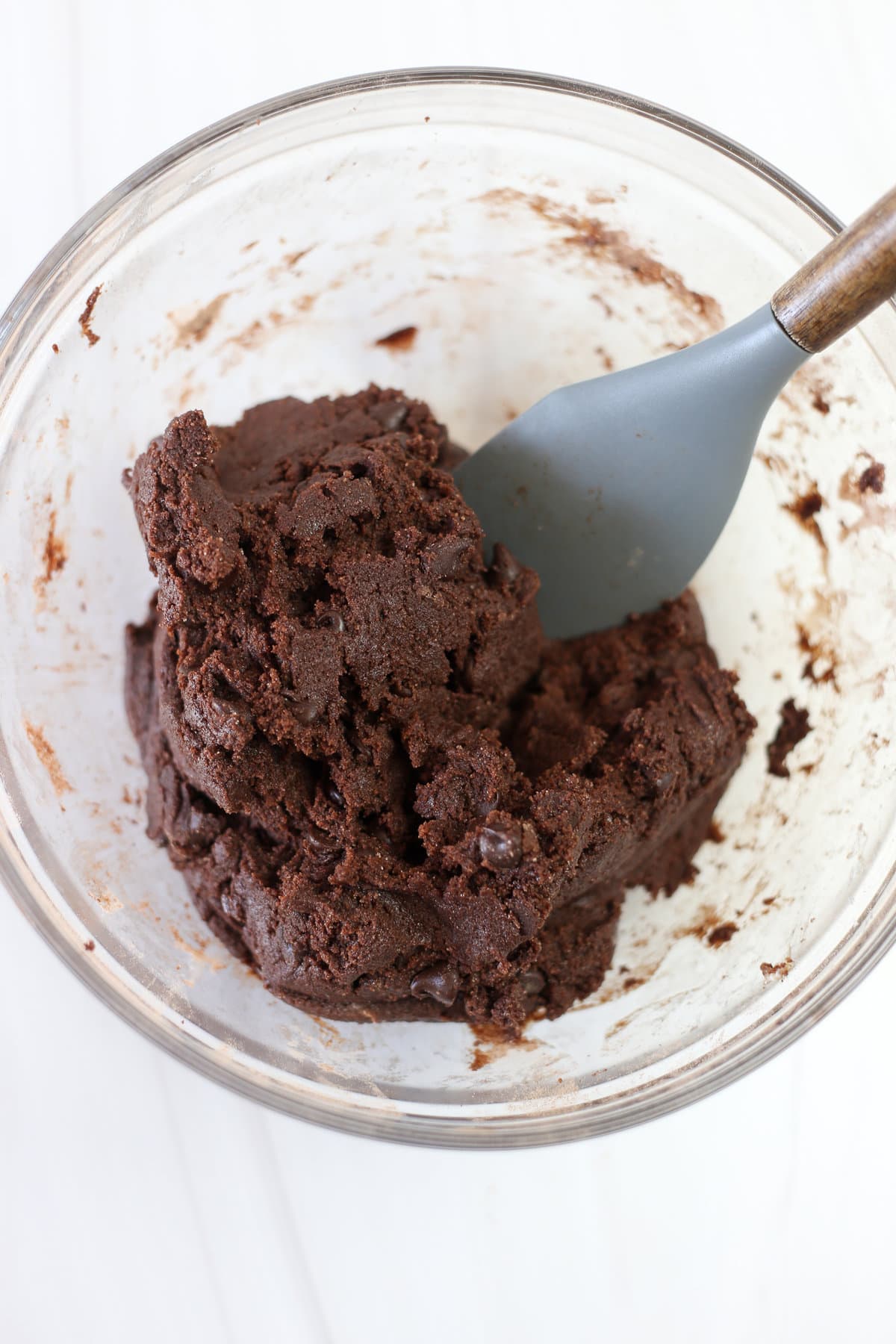 Brownie cookie dough being mixed with a wooden spoon in a glass bowl.