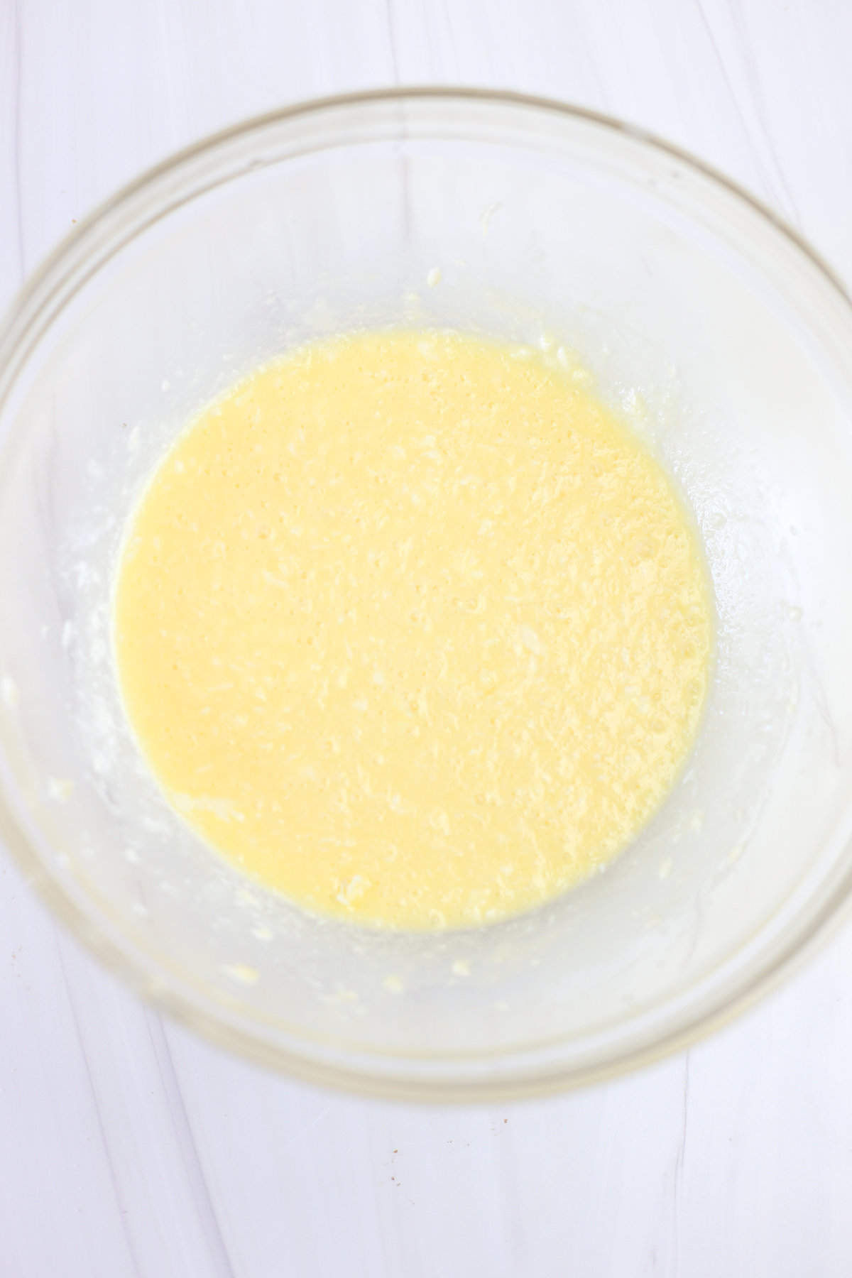 Melted butter, vanilla, water, and eggs mixed together in a glass mixing bowl.