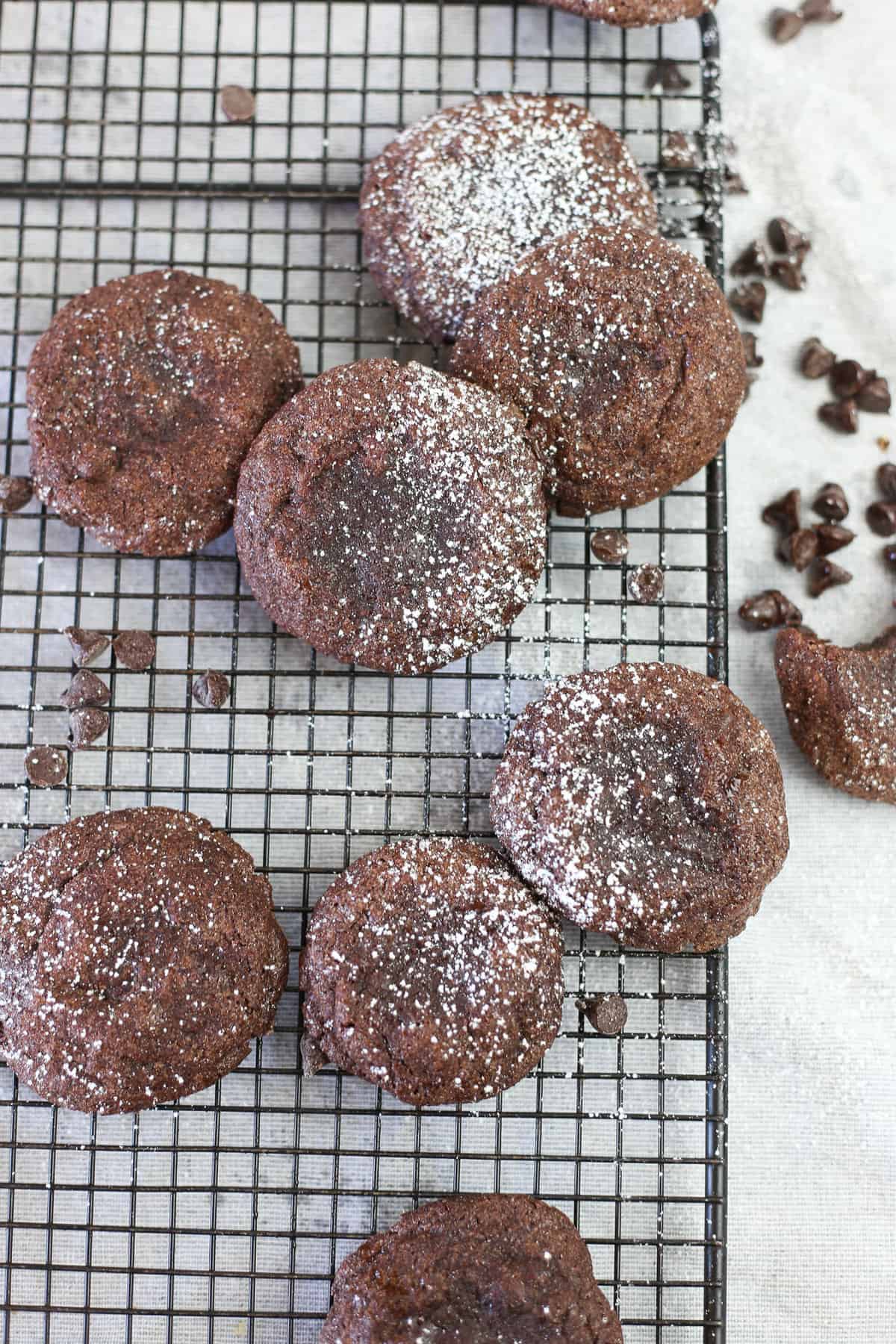 Brownie mix cookies sprinkled with powdered sugar on a cooling rack with chocolate chips around them.