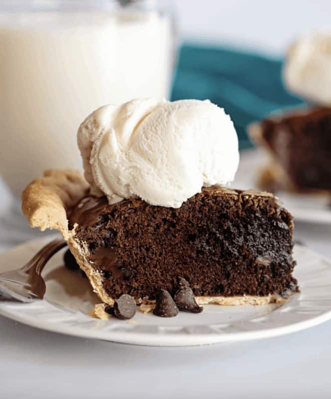 A slice of chocolate brownie pie on a plate with vanilla ice cream on top.