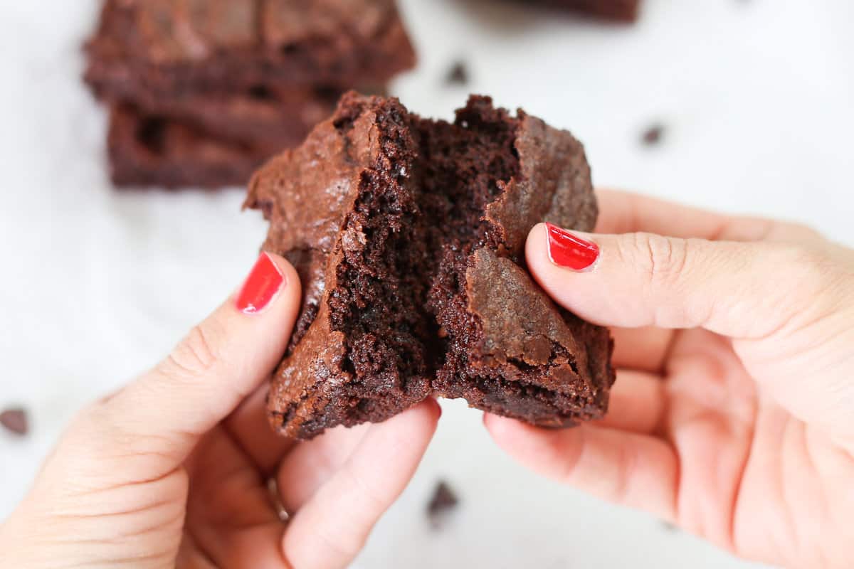 Two hands breaking a brownie in half.