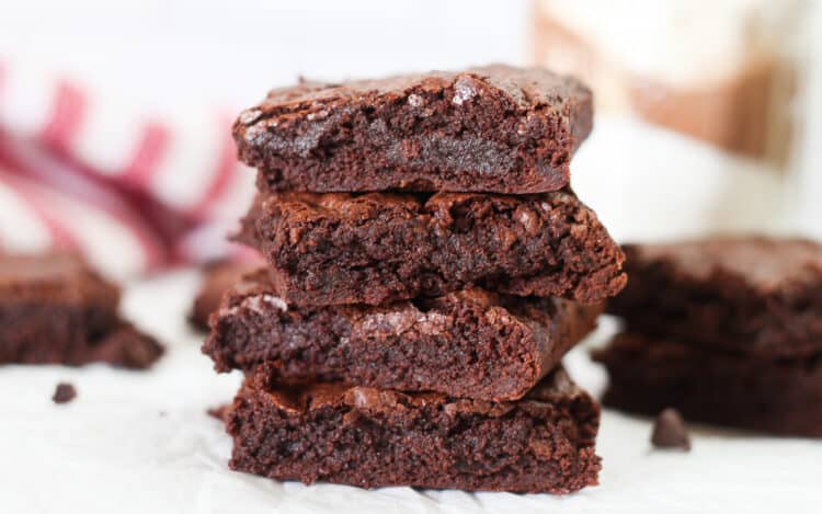 Stack of four brownies with a stack of two brownies next to it and chocolate chips sprinkled around.