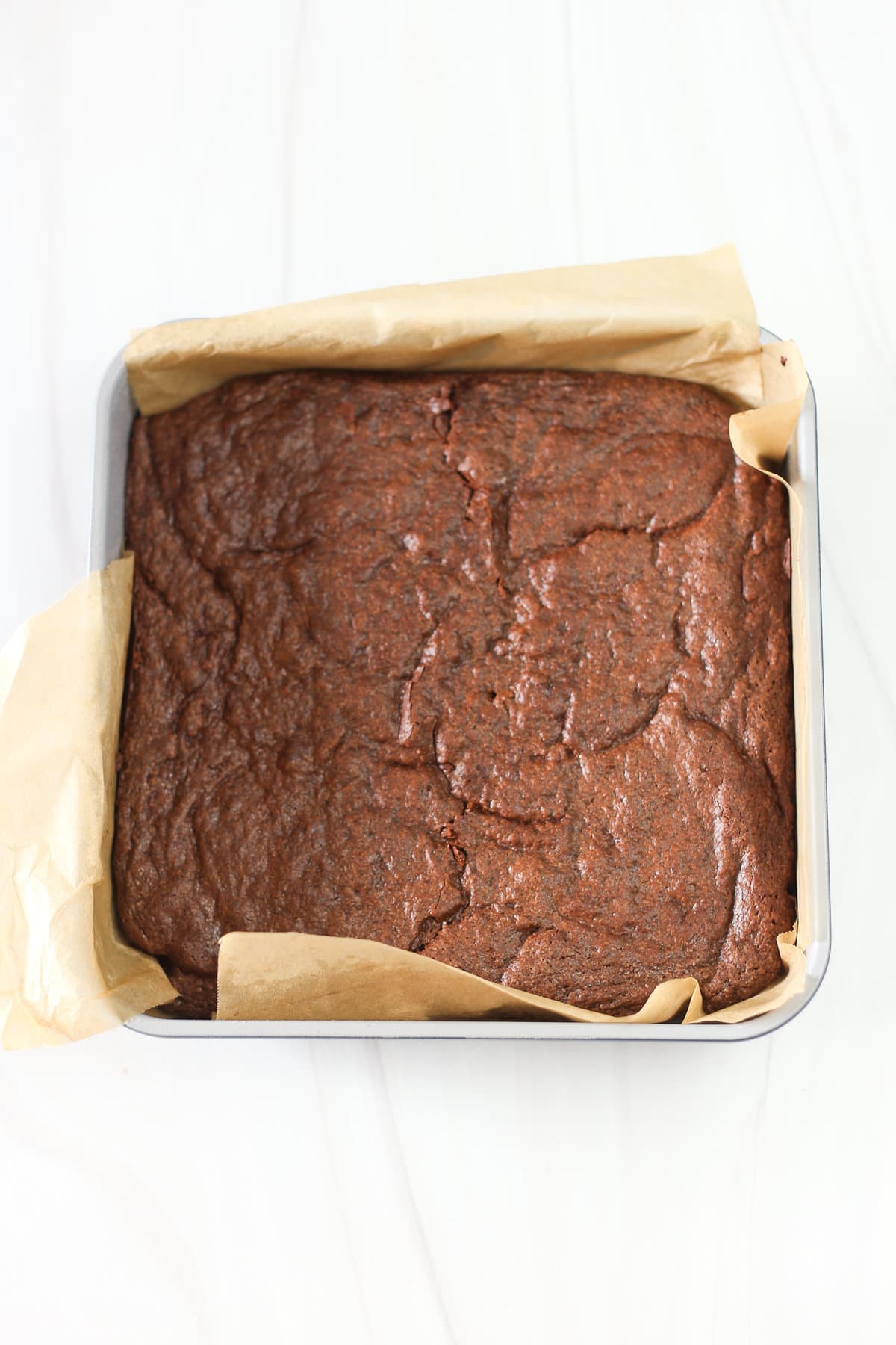 Brownie battered poured into a square pan lined with parchment paper.