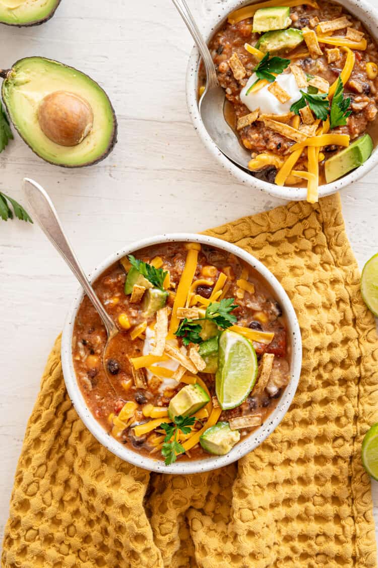 Two bowls of vegetarian tortilla soup with a lime wedge, fresh cilantro, tortilla chips, and a dollop of sour cream on top of both.