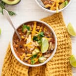 Bowl of easy crockpot vegetarian tortilla soup on a gold tea towel with lime wedges around it.