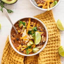 Bowl of easy crockpot vegetarian tortilla soup on a gold tea towel with lime wedges around it.