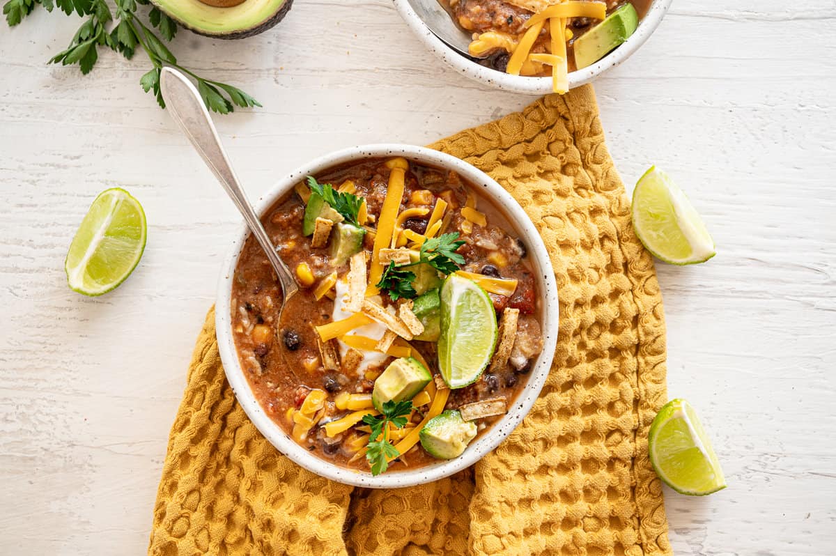 Bowl of vegetarian tortilla soup on a gold tea towel with lime wedges around it.