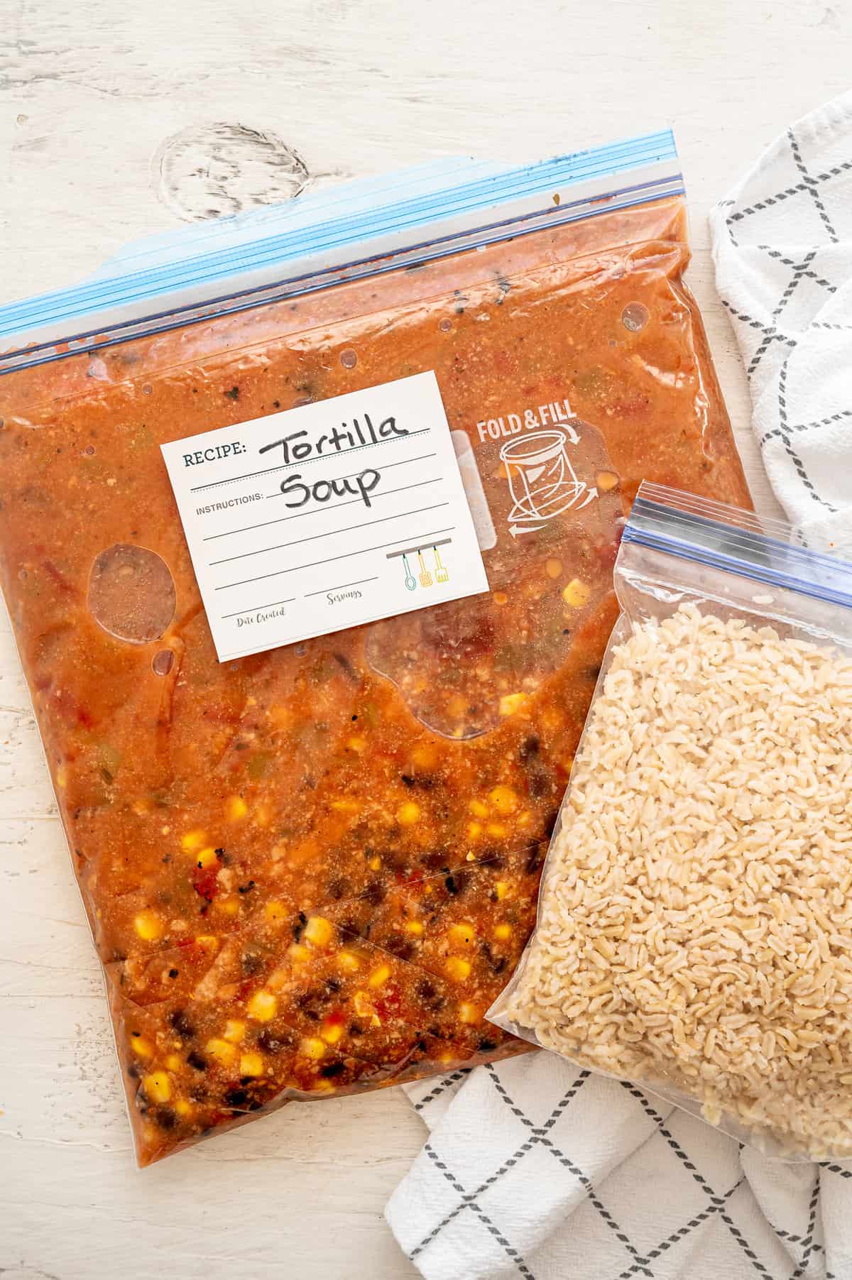 A gallon-sized freezer bag of soup labeled Tortilla Soup and a quart-size freezer bag of cooked rice next to it.