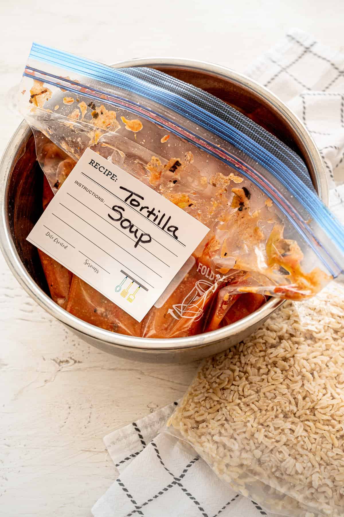 Full freezer bag labeled Tortilla Soup sitting inside an Instant Pot with a bag of rice beside it.