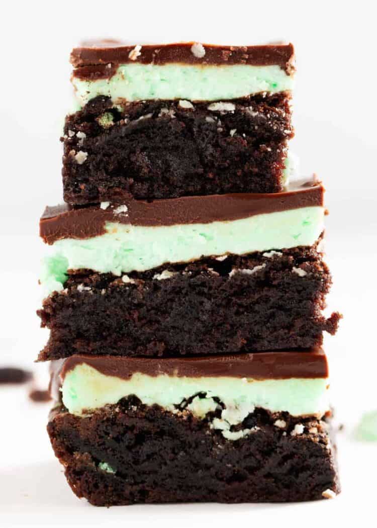 Three mint brownies stacked up showing the layers of brownie, mint frosting, and chocolate ganache.