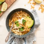 instant pot white chicken chili in a gray bowl with avocado slices, fresh cilantro, tortilla strips, and a dollop of sour cream on top.