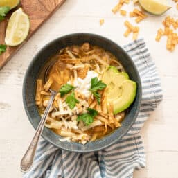 instant pot white chicken chili in a gray bowl with avocado slices, fresh cilantro, tortilla strips, and a dollop of sour cream on top.