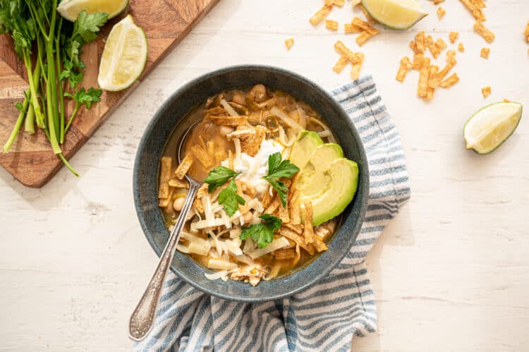 instant pot white chicken chili in a gray bowl with avocado slices, fresh cilantro, tortilla strips, and a dollop of sour cream on top.