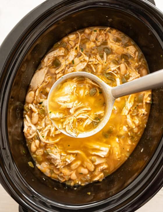 A ladle full of white chicken chili being served from a crock pot.