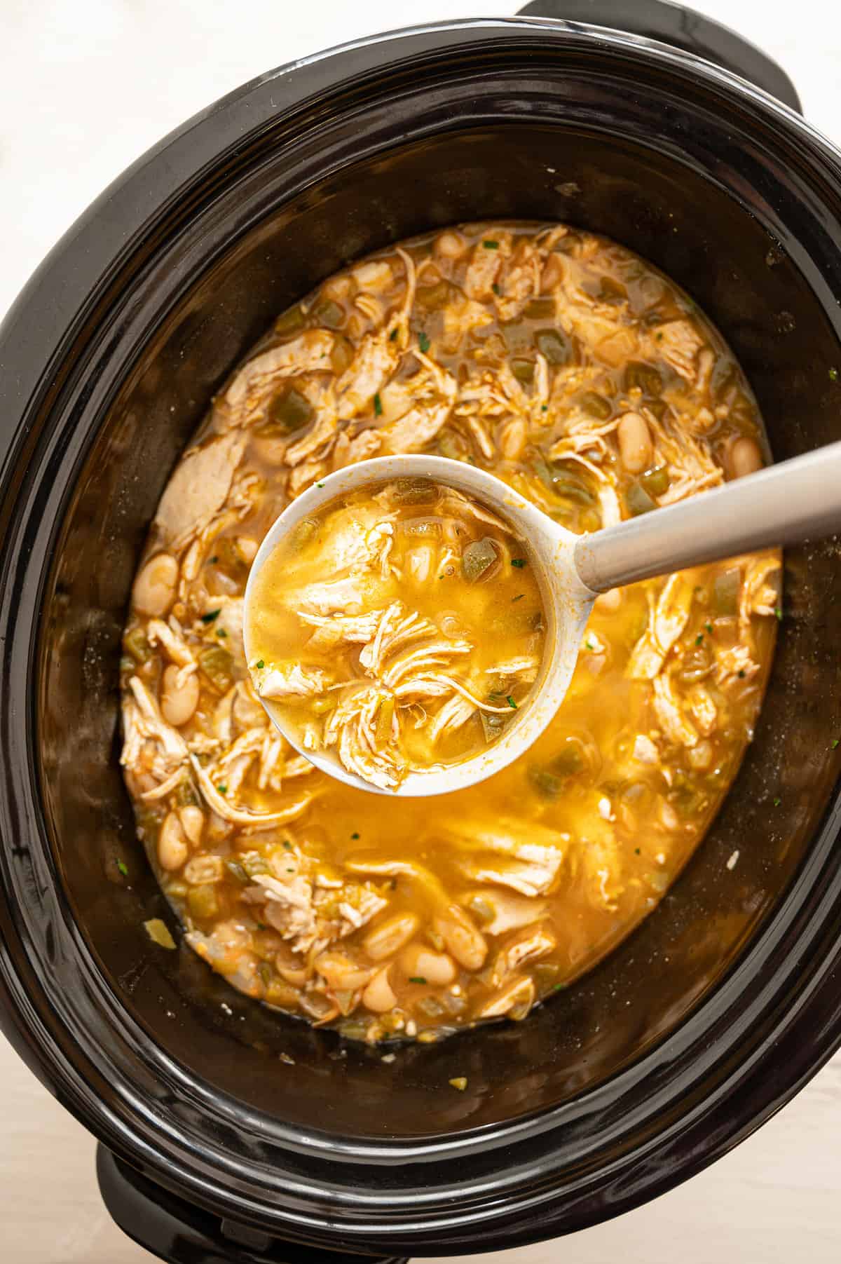 A ladle full of white chicken chili being served from a crock pot.
