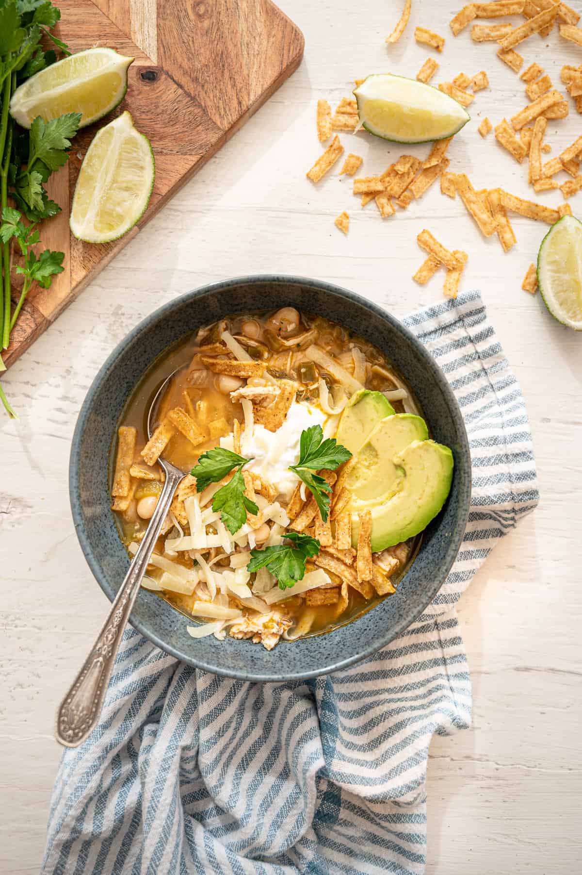 White chicken chili in a gray bowl with avocado slices, a dollop of sour cream, and fresh parsley on top.