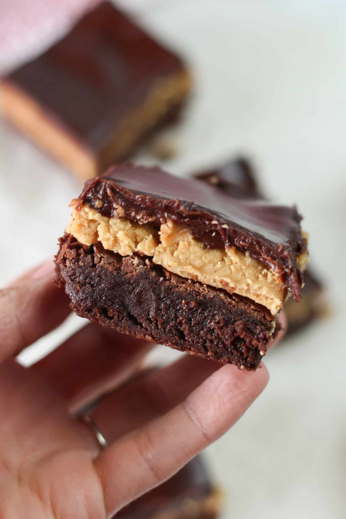Hand holding a buckeye brownie showing all three layers: brownie, peanut butter, and chocolate ganache.