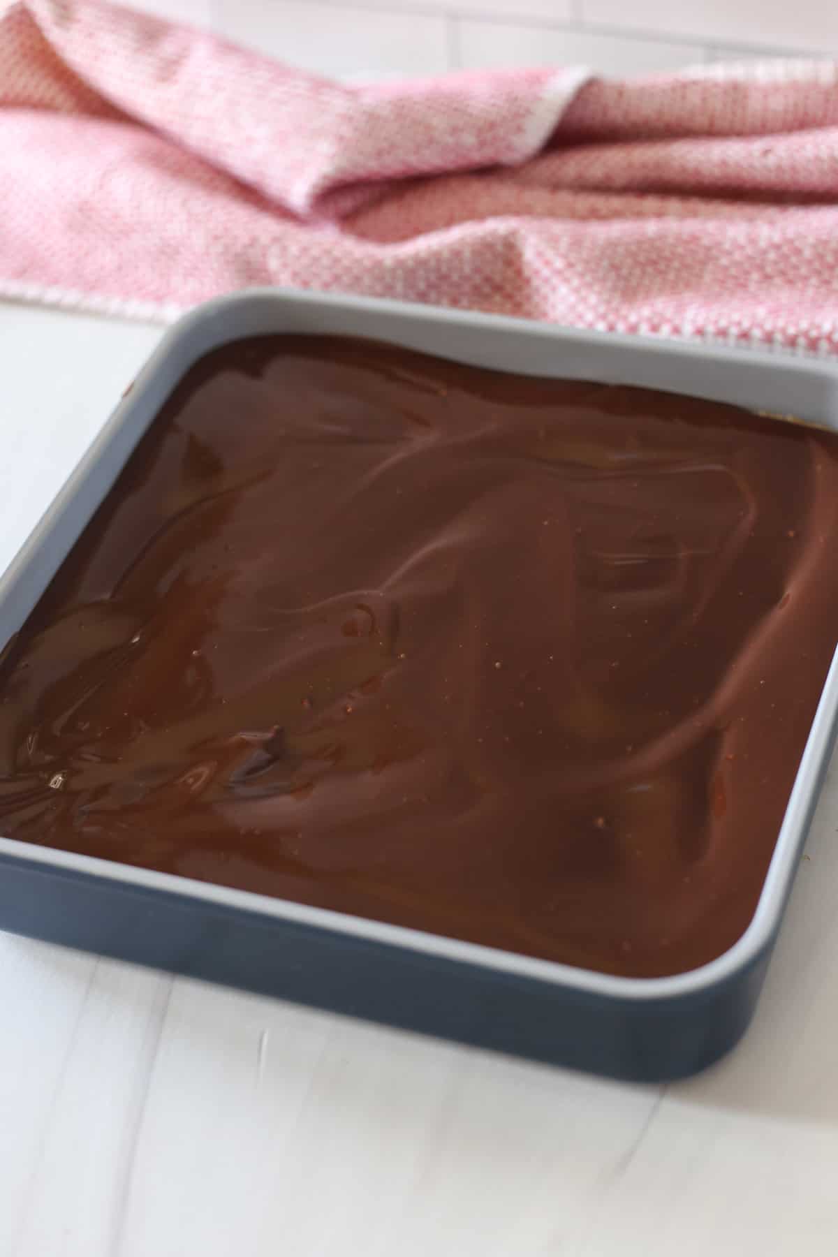 Chocolate Ganache layer spread out in a baking pan on top of brownie and peanut butter layers to make Buckeye Brownies.