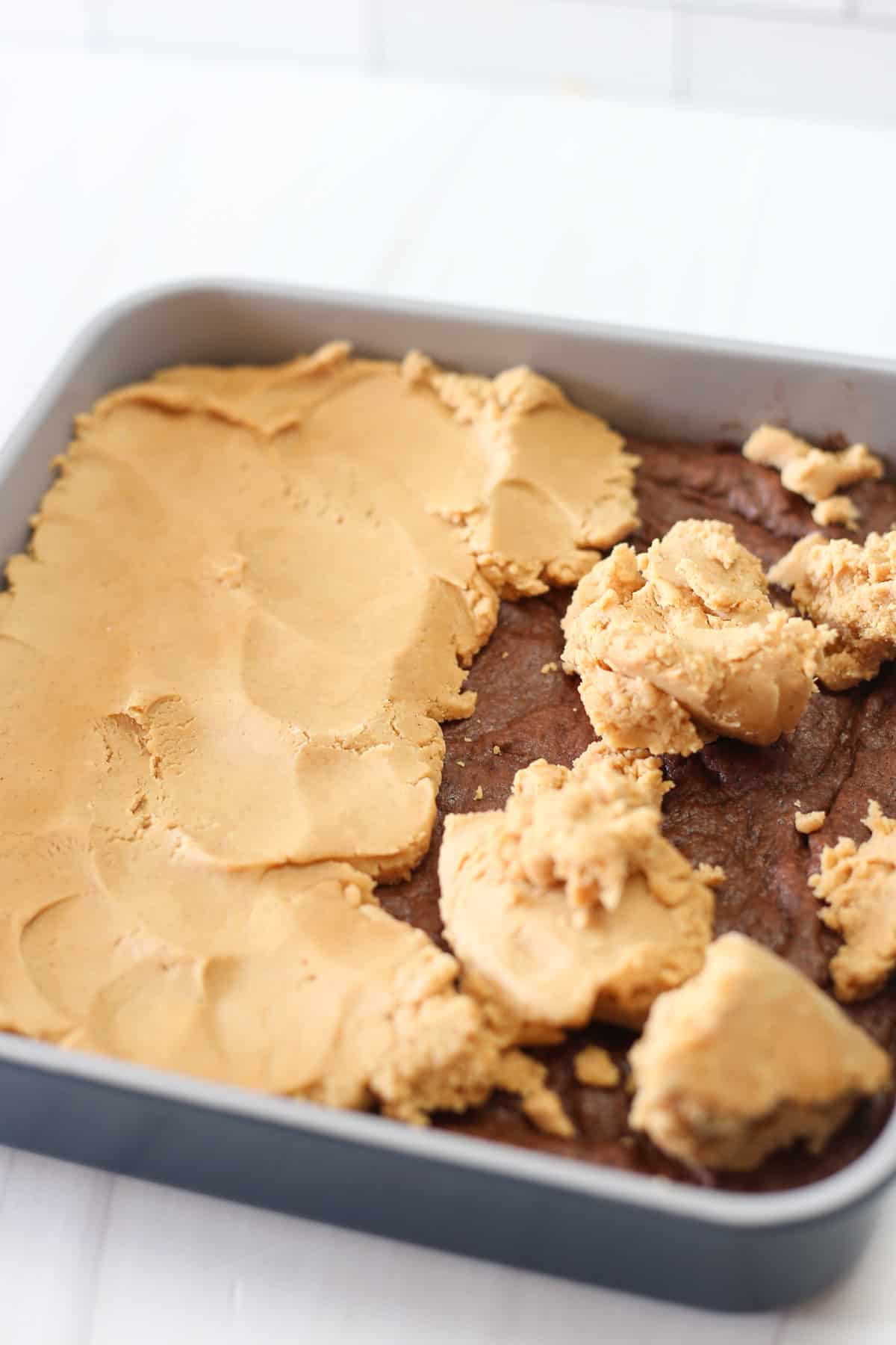 Peanut butter layer being spread out on top of brownies in a pan for Buckeye Brownies.