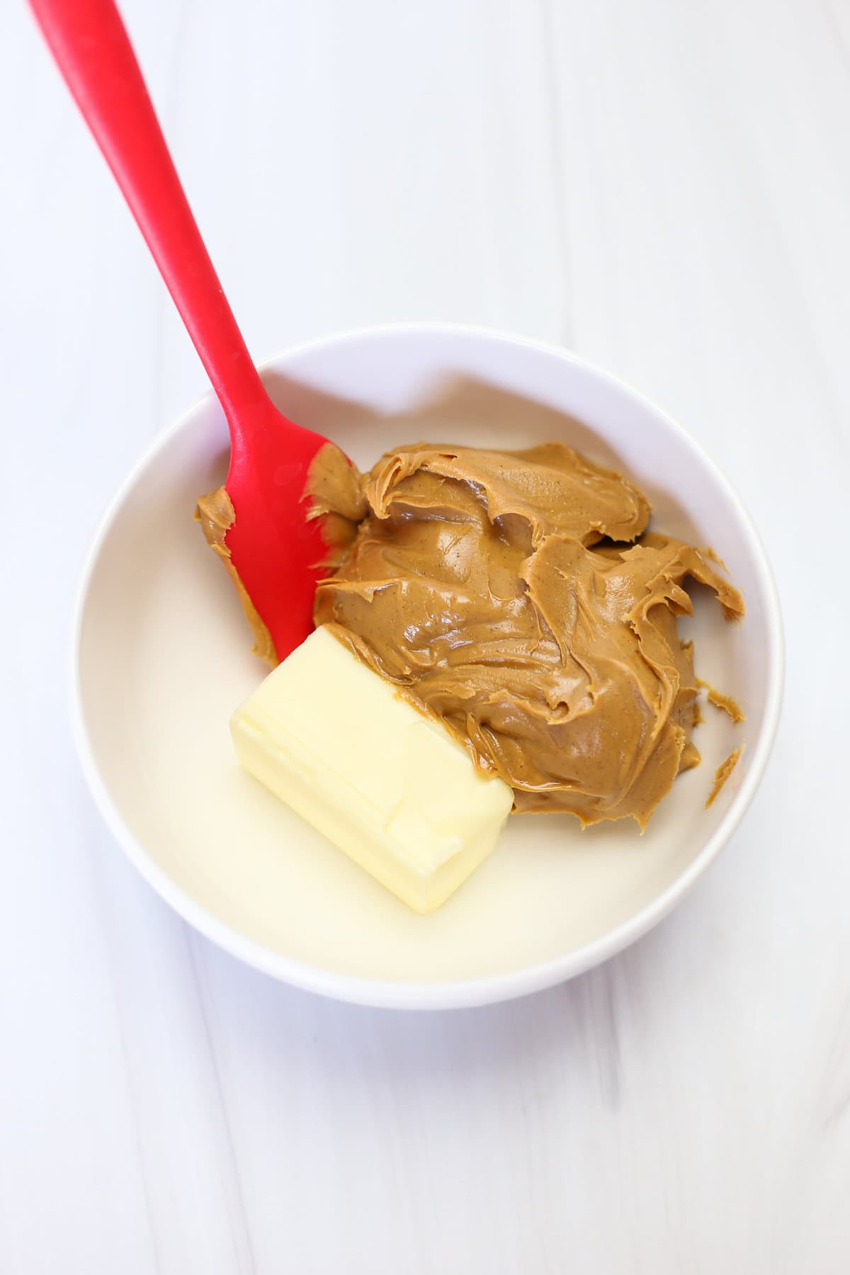 Peanut butter and softened butter in a small bowl being mixed with a red spatula.