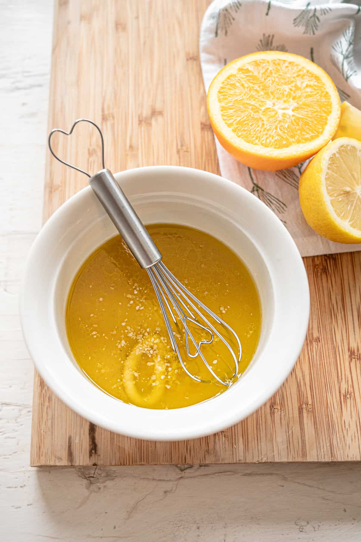 Creamy citrus dressing ingredients being whisked together with a small wire whisk in a white bowl.