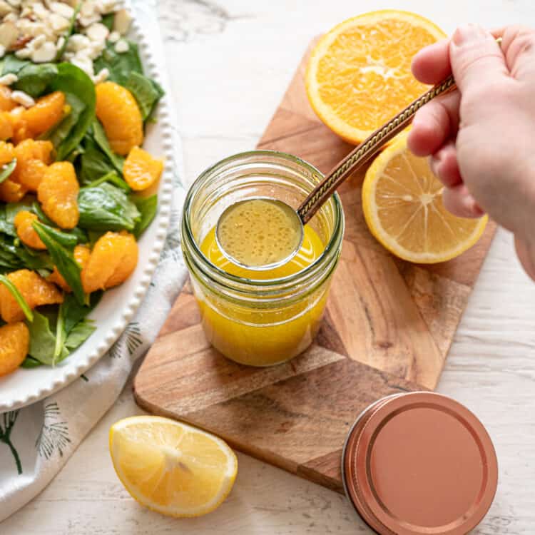 Homemade creamy citrus dressing in a small jar being ladled onto a Mandarin orange salad next to it.
