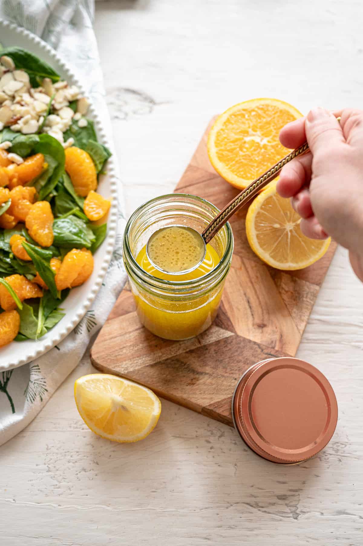 Homemade creamy citrus salad dressing in a small jar being ladled onto a Mandarin orange salad next to it.
