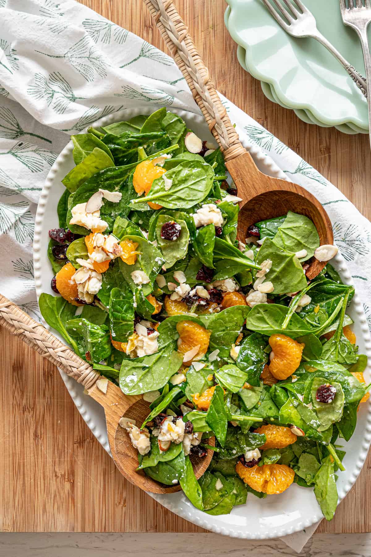 Mandarin orange spinach salad ingredients including sliced almonds, feta cheese, and dried cranberries tossed in a creamy citrus dressing on a white platter.