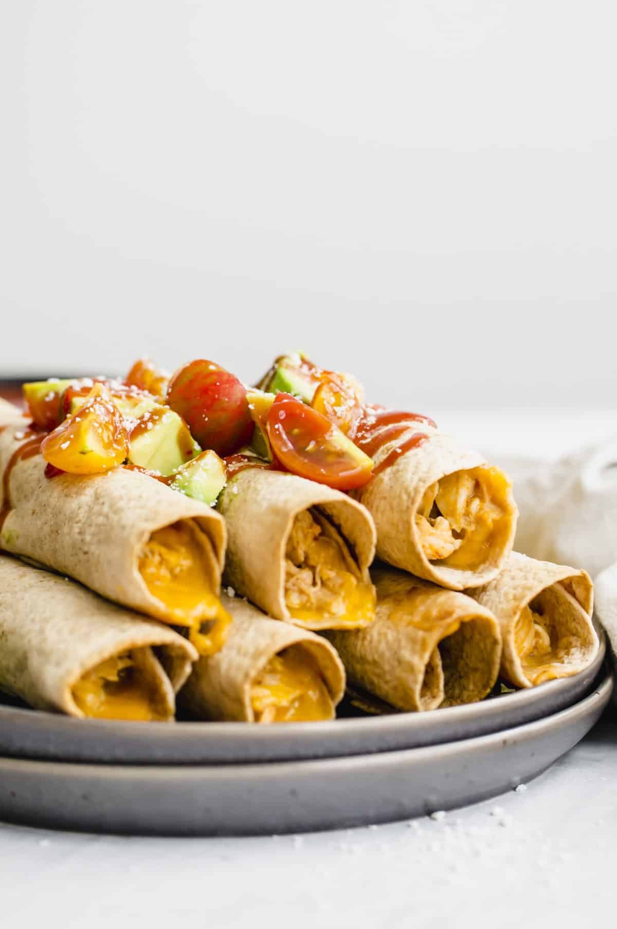 Side view of chicken and cheese taquitos with salsa on top.