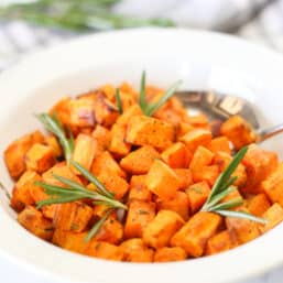 Air fryer sweet potato cubes in a white bowl with sprigs of rosemary.