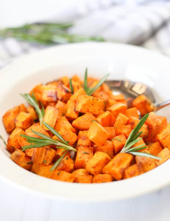Air fryer sweet potato cubes in a white bowl with sprigs of rosemary.