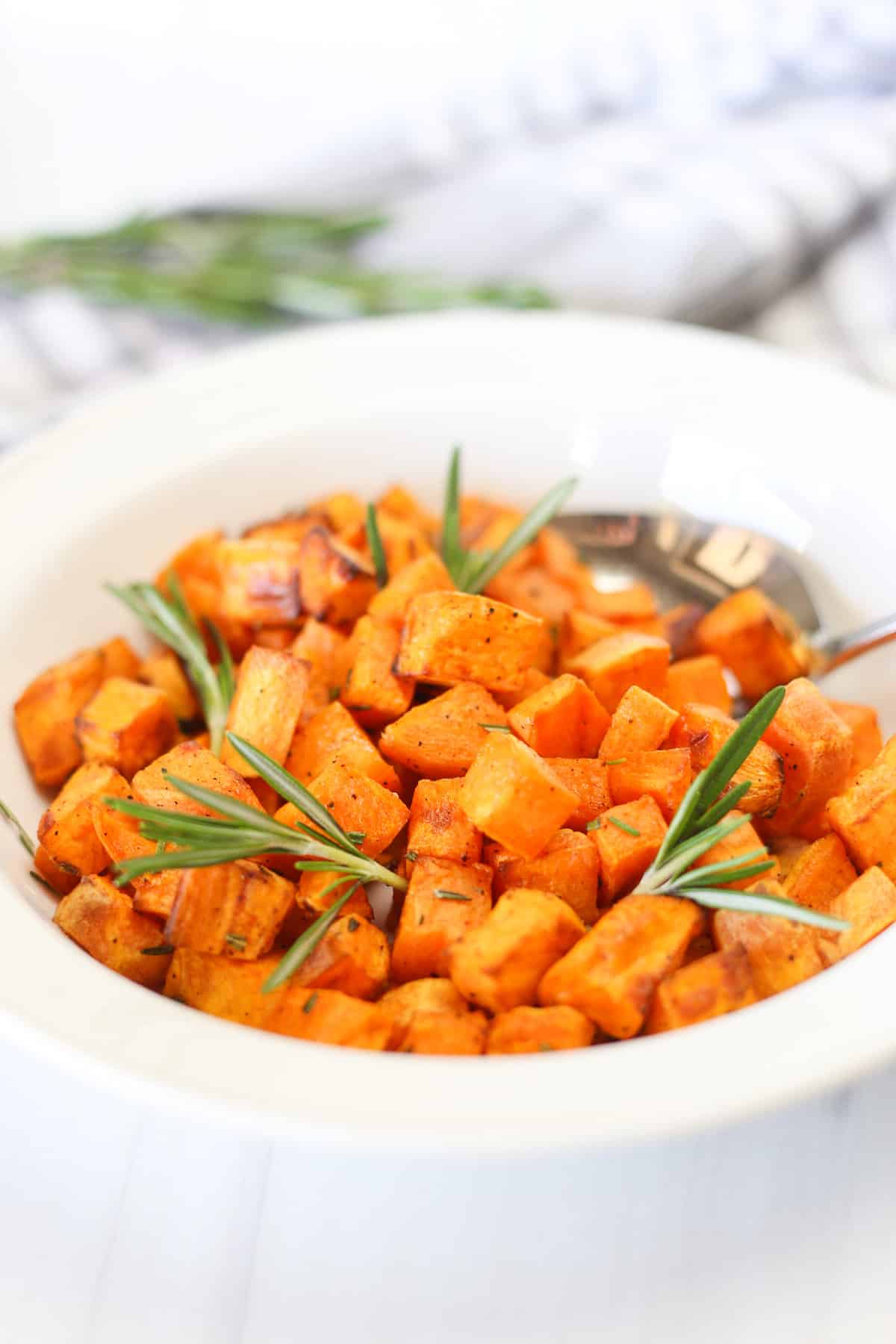 Air fryer sweet potato cubes in a white bowl with sprigs of rosemary. 