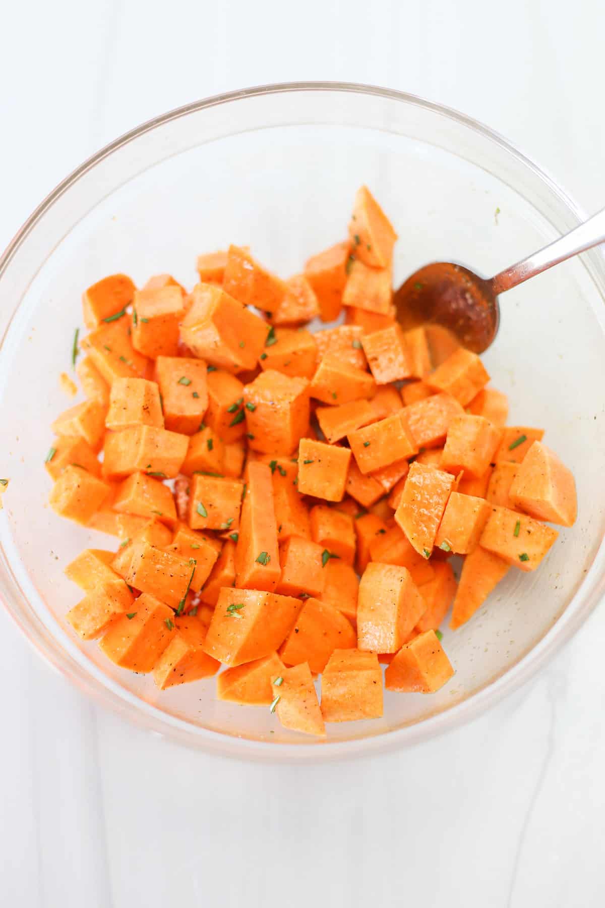 A large bowl with sweet potato cubes being tossed in oil and prepped for the air fryer.