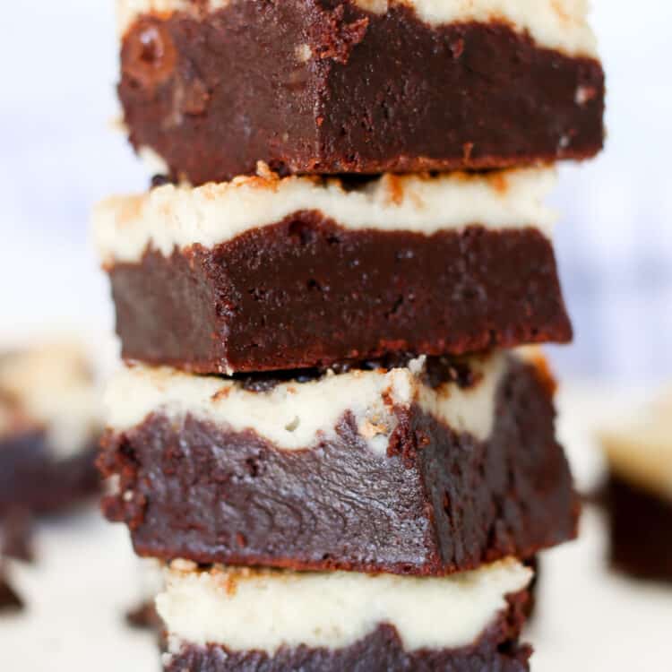 Chocolate chip cheesecake brownies stacked on top of each other witch chocolate chips sprinkled around.
