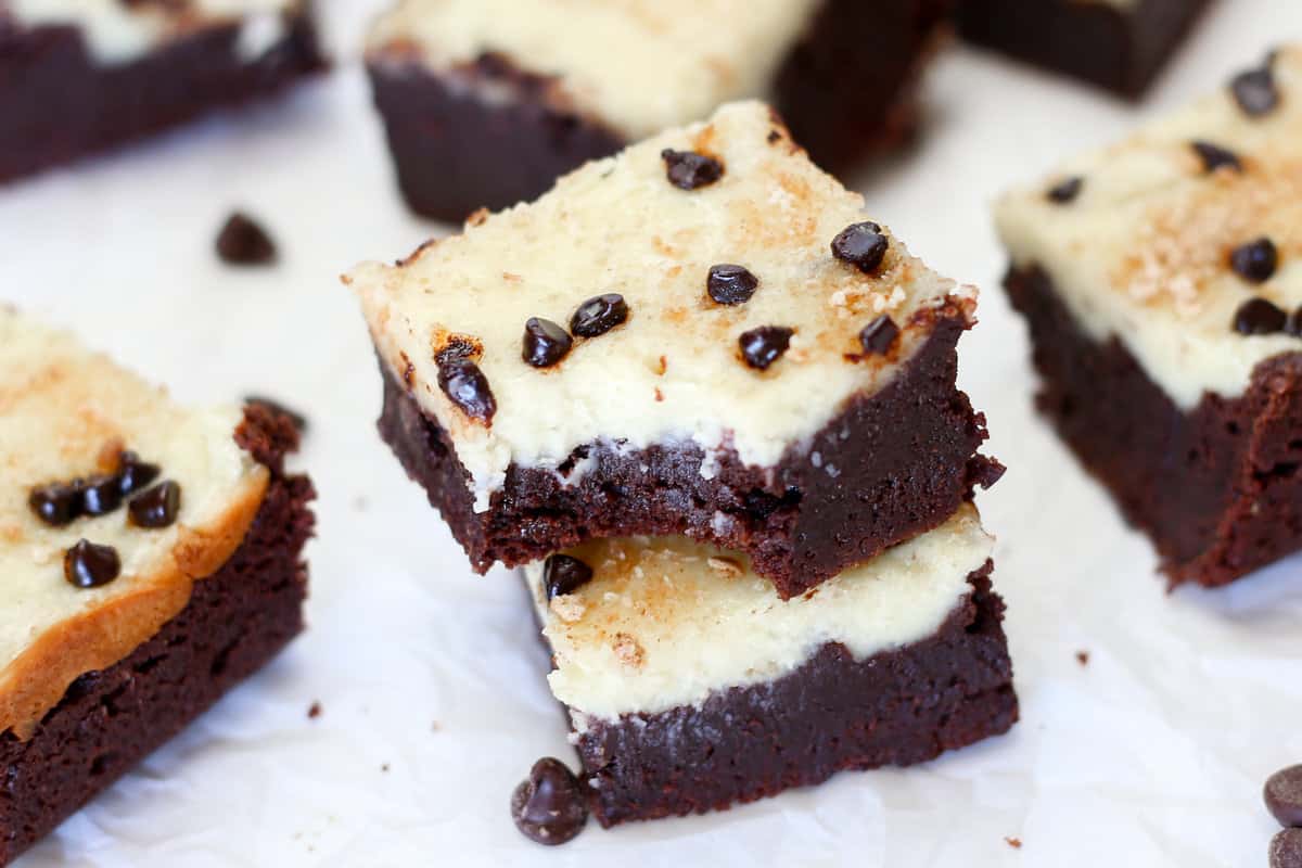 Several chocolate chip cheesecake brownies on parchment paper with one missing a bite.