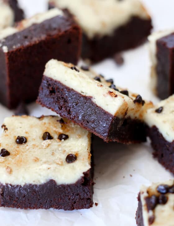A bunch of chocolate chip cheesecake brownies scattered around on parchment paper.
