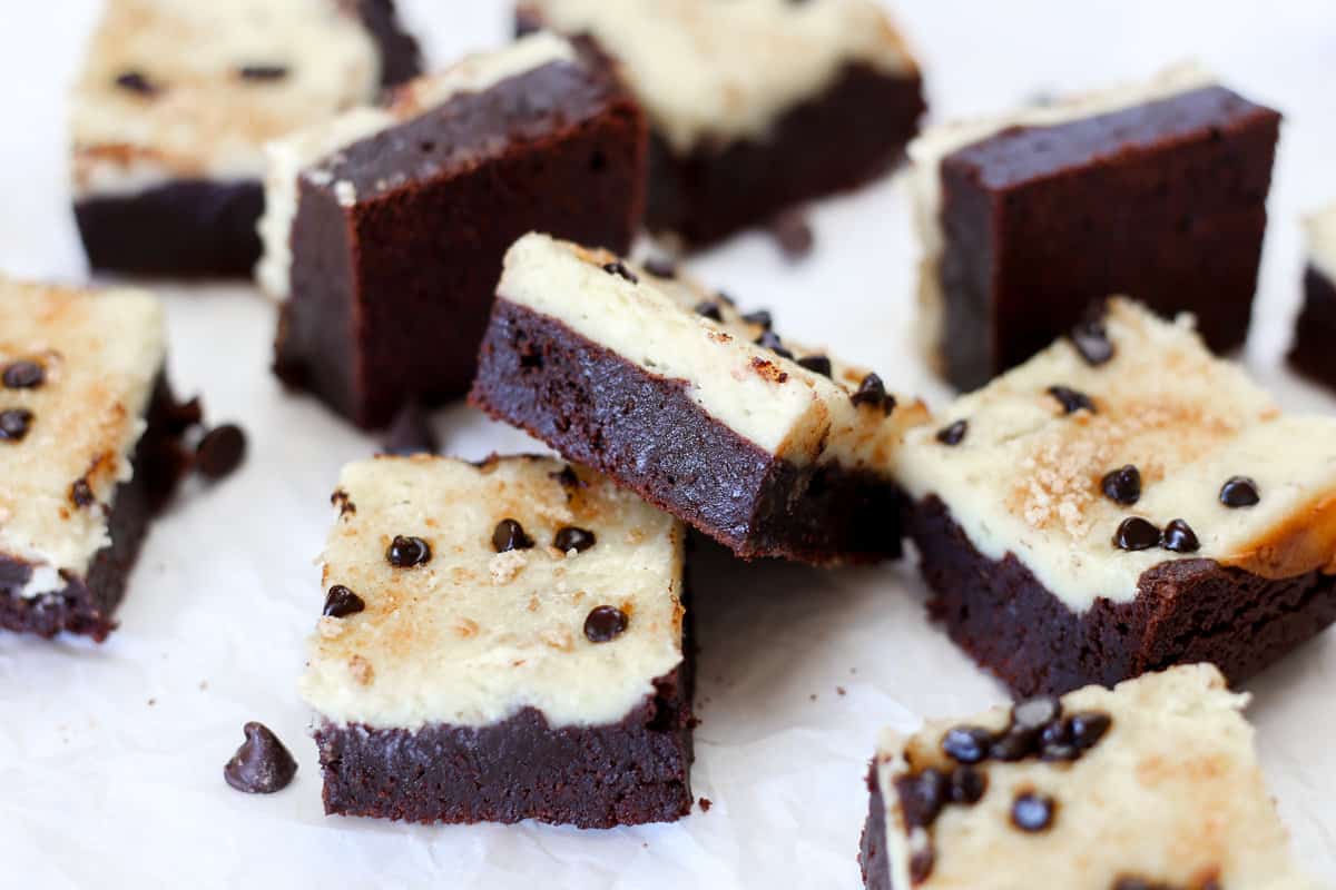 A bunch of chocolate chip cheesecake brownies scattered around on parchment paper.